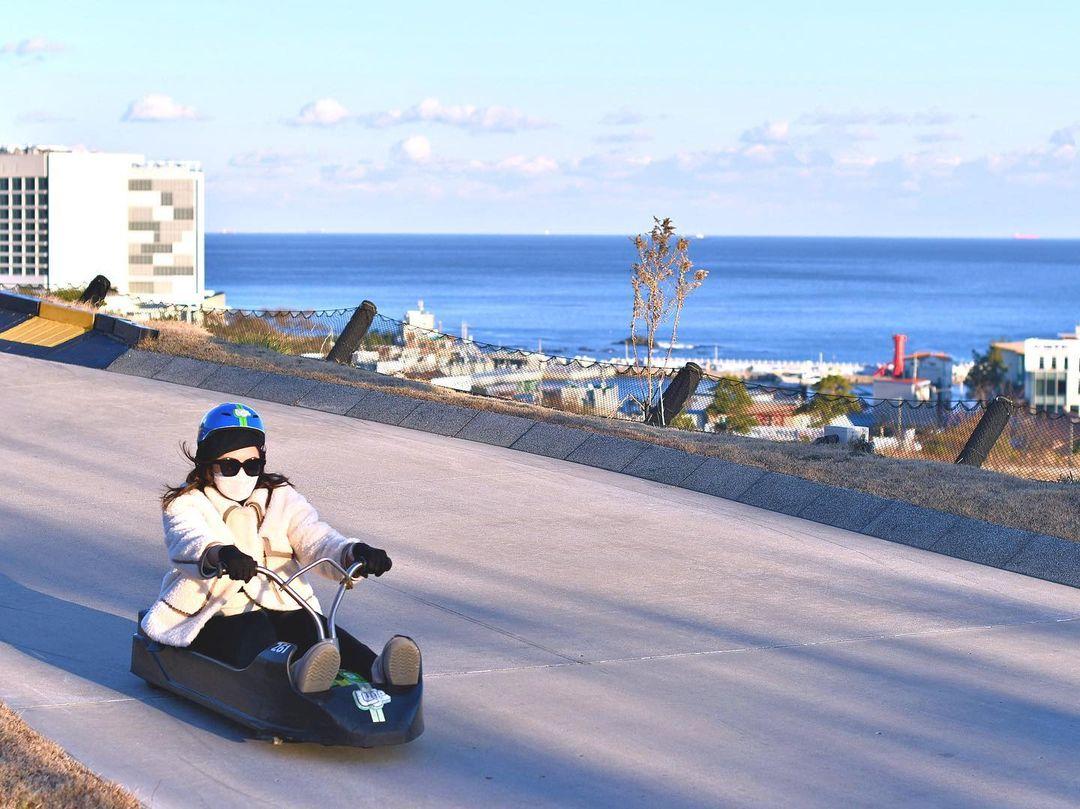 A lady rides the Busan Luge with stunning views of the Dong Busan beach behind her.