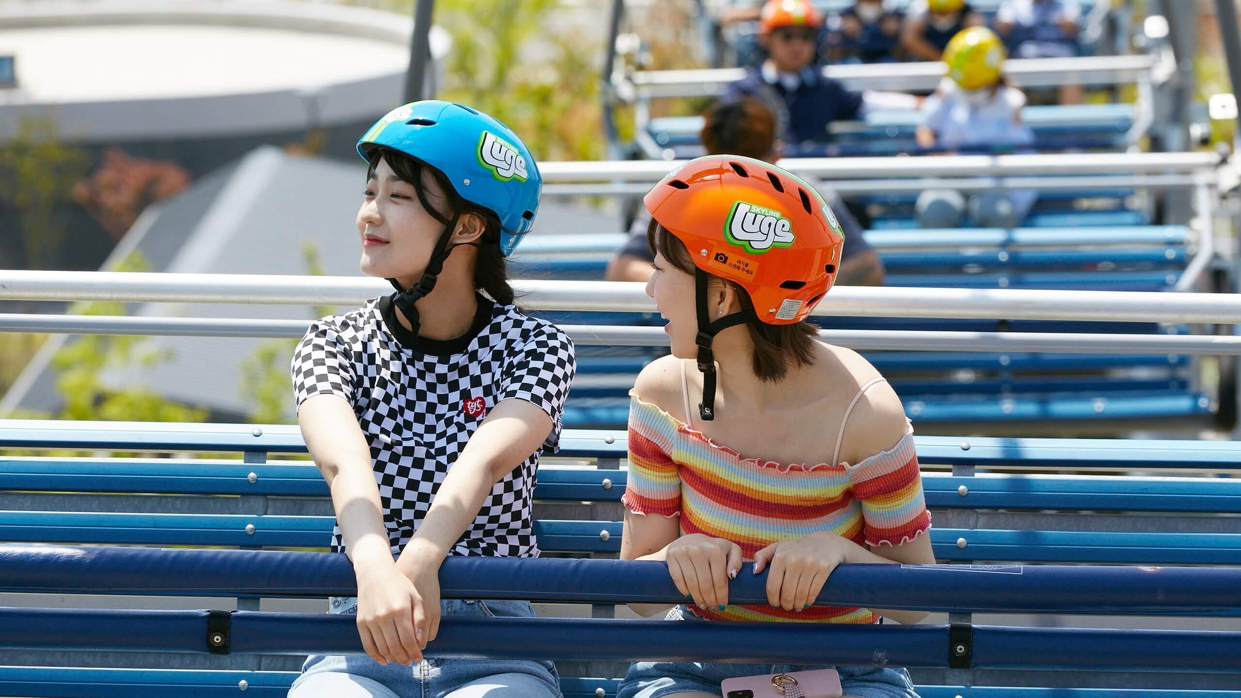 Two friends laugh while riding the Skyline Luge Busan chairlift.